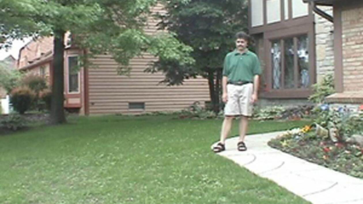 A man standing on lawn with a house in the background.