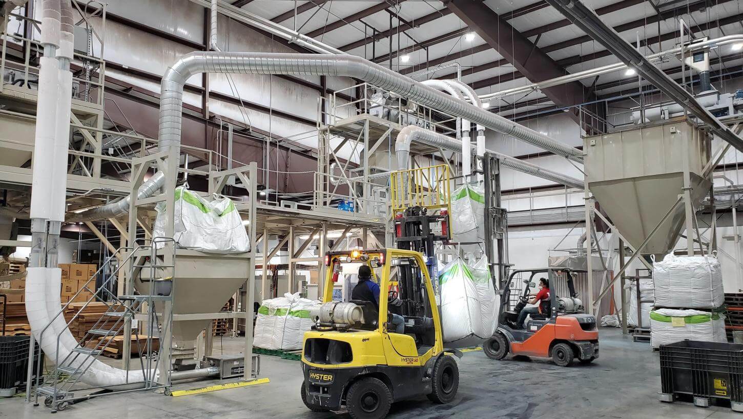 Factory floor with two forklifts driving around.