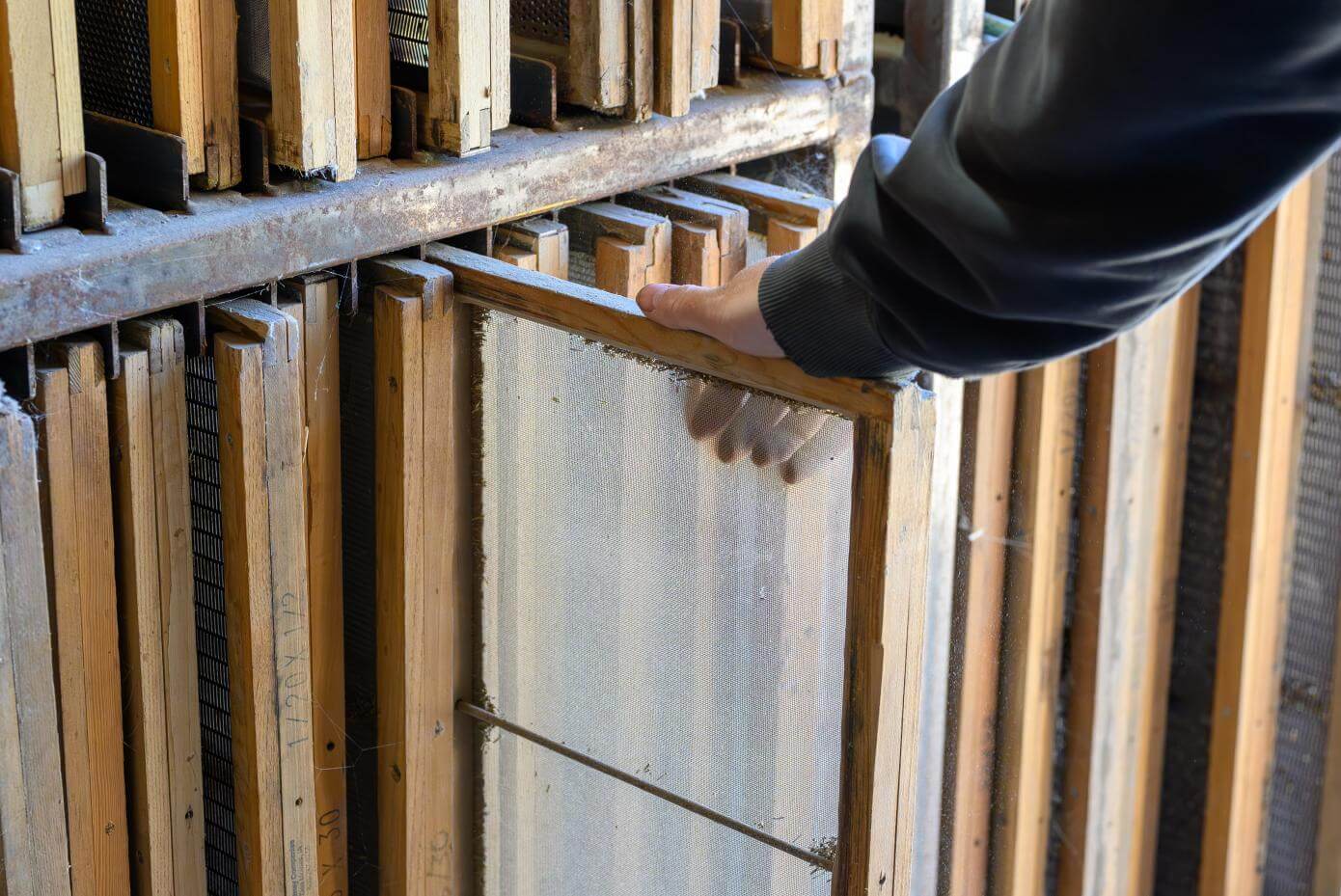 A man's hand grabbing a wooden framed screen out of a shelf with other wooden framed screens.